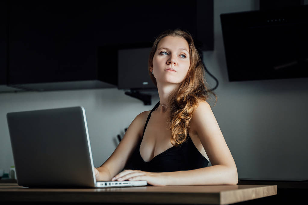 Joven chica triste hermosa se sienta en una mesa delante de un ordenador portátil y
 - Foto, Imagen