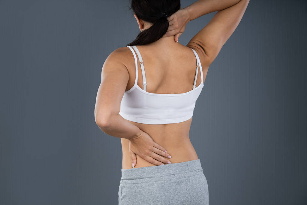 Женщина, страдающая от боли в спине на сером фоне
 - Фото, изображение