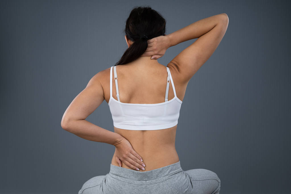 Женщина, страдающая от боли в спине на сером фоне
 - Фото, изображение