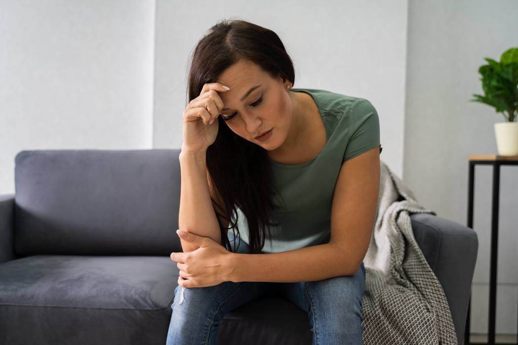 Молода депресивна жінка сидить на дивані вдома
 - Фото, зображення