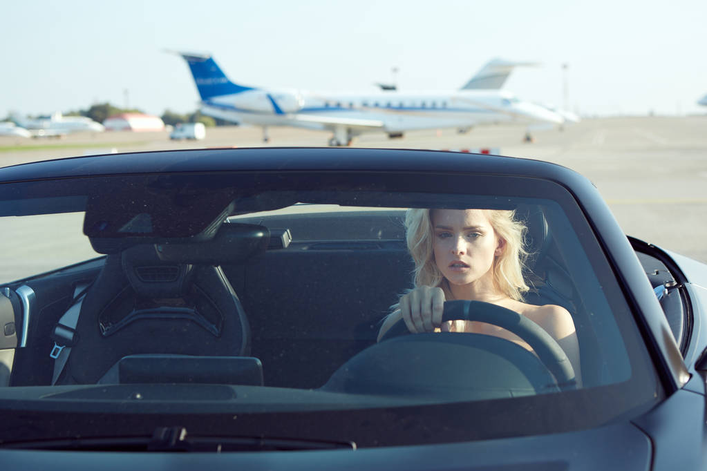 Eine glamouröse blonde Frau sitzt im Cabriolet-Auto, Glamour-Girl im Cabrio-Auto auf dem Laufsteg. Keine Retusche. - Foto, Bild