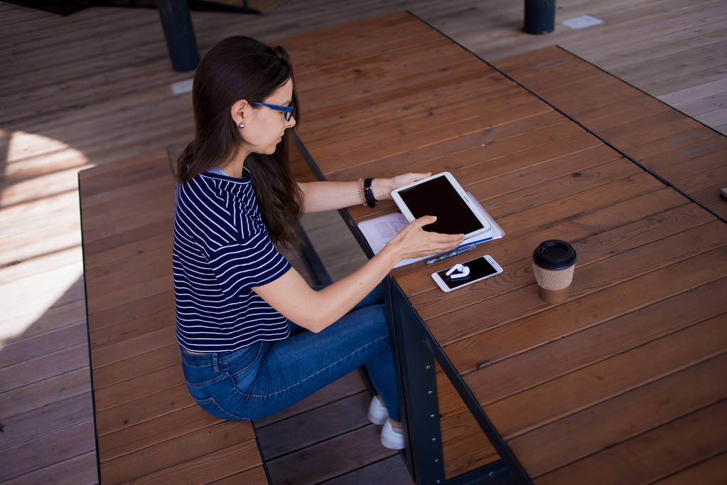 Ciddi bir esmer kız, freelancer, büyük kol saati ile, tablet ahşap bir masada çalışır, gadget'lar ve kağıtları ile. - Fotoğraf, Görsel