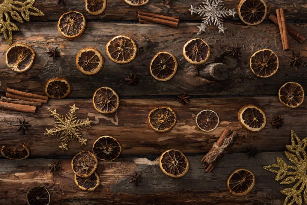 вид зверху сушені цитрусові скибочки з анісом, паличками кориці та декоративними сніжинками на дерев'яному фоні
 - Фото, зображення