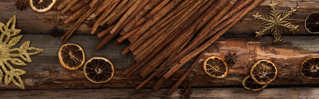 felülnézetből fahéjas rudak közelében ánizs, szárított citrusszeletek és hópelyhek fából készült háttér, panorámás lövés - Fotó, kép