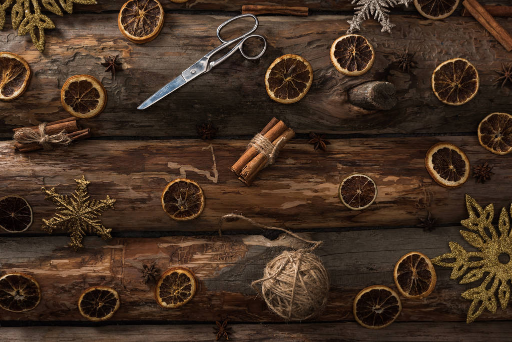 vista superior de paus de canela, anis, fatias de citrinos secos, tesoura, bola de linha e flocos de neve em fundo de madeira
 - Foto, Imagem