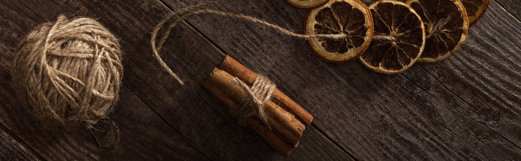 vrchní pohled na sušené citrusové plátky na laně u skořice na dřevěném povrchu, panoramatický záběr - Fotografie, Obrázek