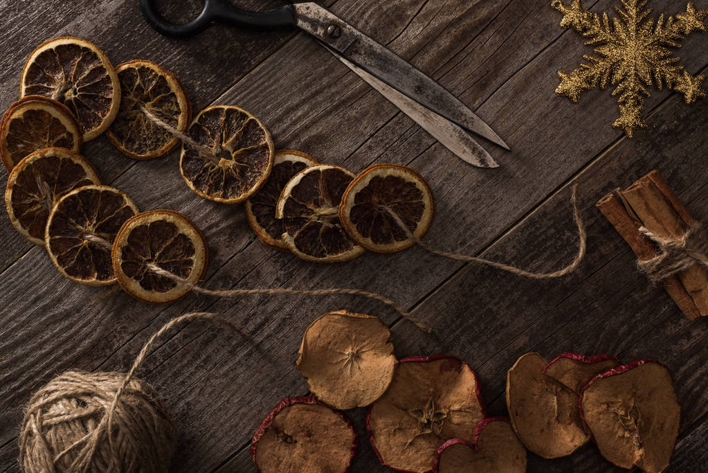 vrchní pohled na sušené citrusy a jablečné plátky v blízkosti sněhové vločky, skořice, provazu a nůžek na dřevěném povrchu - Fotografie, Obrázek