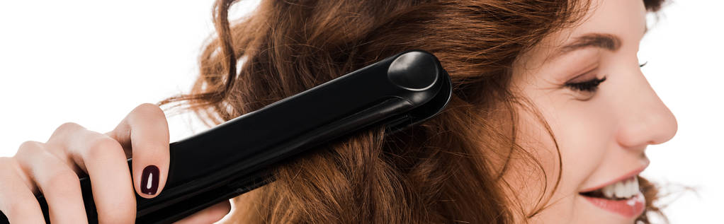 panoramic shot of beautiful curly woman using hair straightener isolated on white   - 写真・画像
