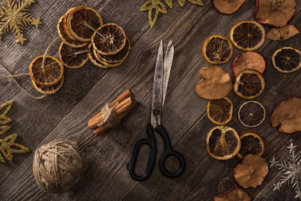 top view of dried citrus and apple slices near snowflakes, scissors, thread and cinnamon on wooden surface - Photo, Image