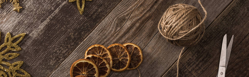 top view of dried citrus slices near snowflakes, thread, scissors on wooden surface, panoramic shot - 写真・画像