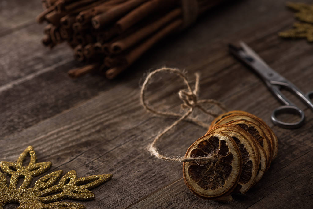 selective focus of dried citrus slices on thread near cinnamon, scissors and snowflake on wooden background - Photo, Image
