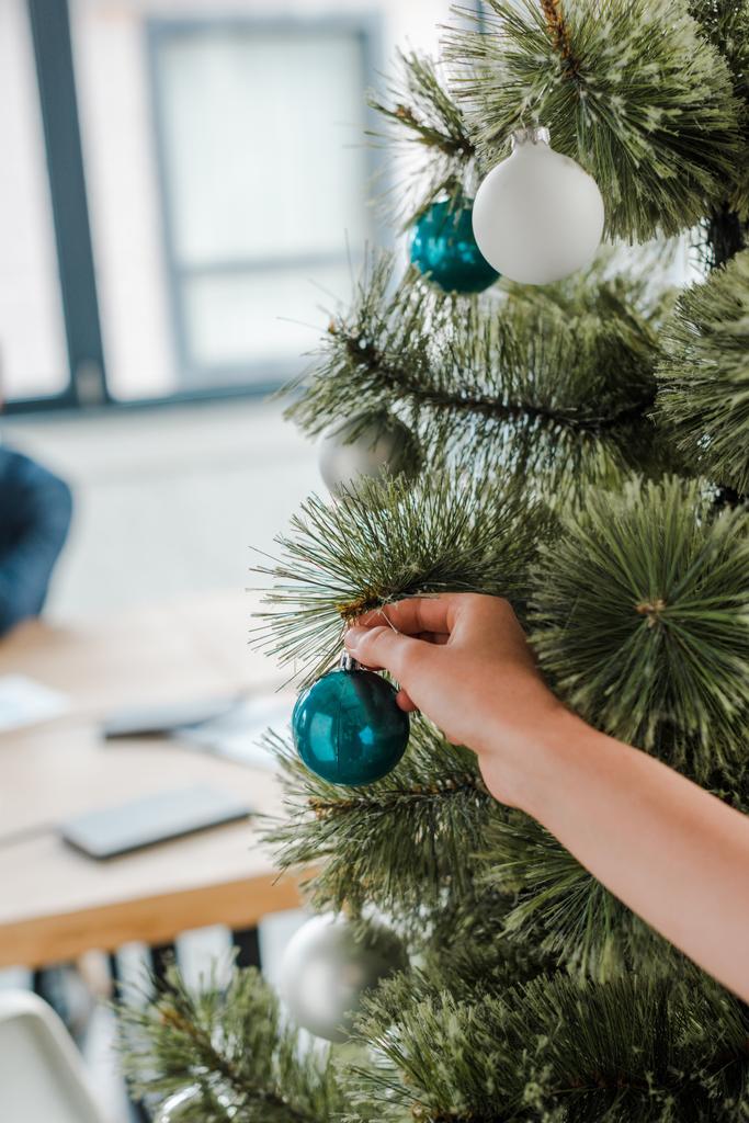περικοπή άποψη της γυναίκας αγγίζοντας χριστουγεννιάτικη μπάλα στο χριστουγεννιάτικο δέντρο στο γραφείο  - Φωτογραφία, εικόνα