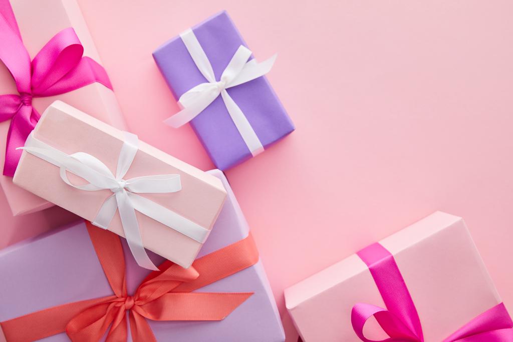 bovenaanzicht van kleurrijke geschenkdozen met linten en strikken verspreid over roze achtergrond - Foto, afbeelding