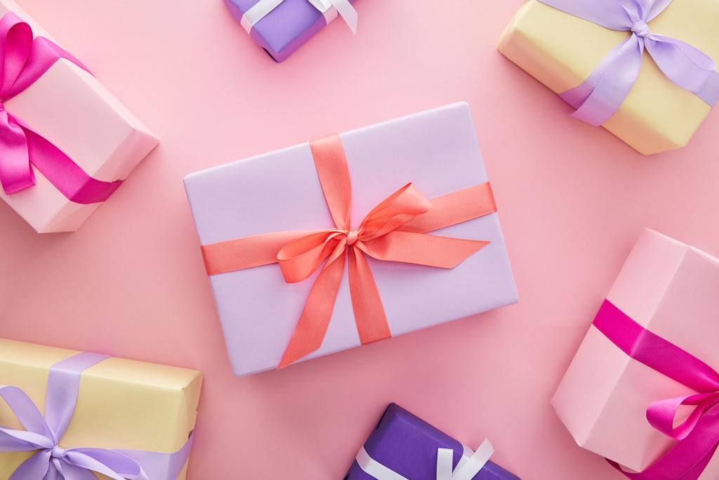 πάνω όψη πολύχρωμα κουτιά δώρων με κορδέλες και φιόγκους σε ροζ φόντο - Φωτογραφία, εικόνα