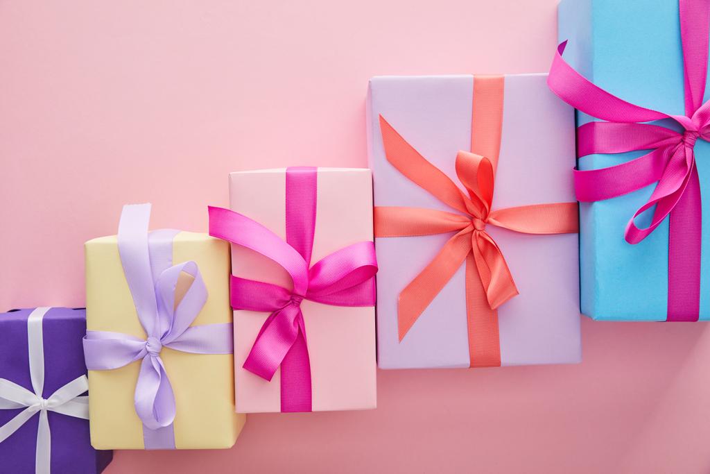 flache Lage mit bunten Geschenkboxen mit Bändern und Schleifen auf rosa Hintergrund mit Kopierraum verstreut - Foto, Bild