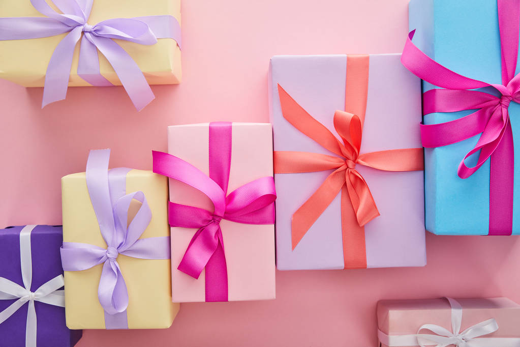 επίπεδο θέσει με πολύχρωμα κουτιά δώρων με κορδέλες και τόξα διάσπαρτα σε ροζ φόντο - Φωτογραφία, εικόνα