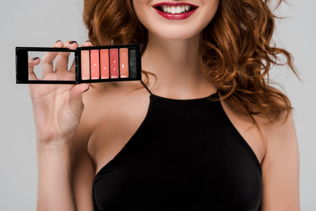 cropped view of happy woman holding set of lip gloss isolated on grey  - Photo, Image