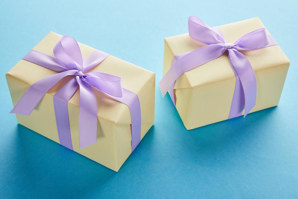 κίτρινα πολύχρωμα κουτιά δώρου με βιολετί κορδέλες και φιόγκους σε μπλε φόντο - Φωτογραφία, εικόνα