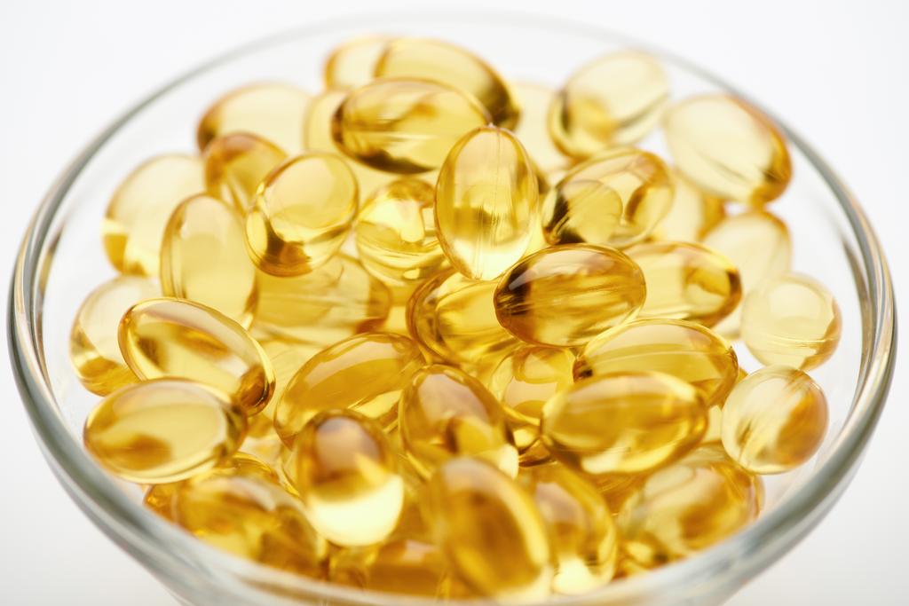 close-up blik op gouden visolie capsules in glazen schaal op witte achtergrond - Foto, afbeelding