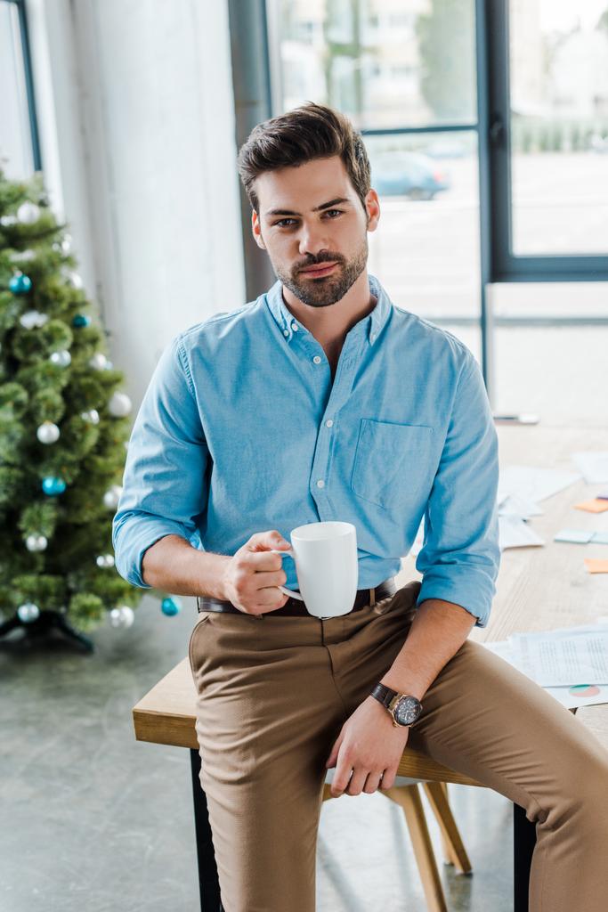 selective focus of bearded man holding cup near christmas tree in office  - Photo, Image