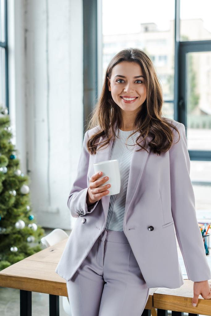 happy businesswoman holding cup near decorated christmas tree  - Photo, Image