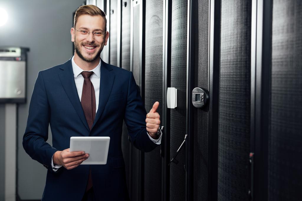 selective focus of cheerful businessman holding digital tablet and showing thumb up in data center  - Photo, Image