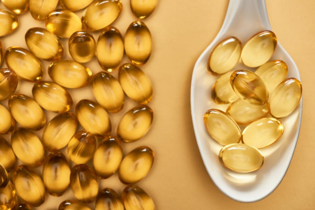 vista dall'alto d'oro lucido capsule di olio di pesce in cucchiaio su sfondo giallo
 - Foto, immagini