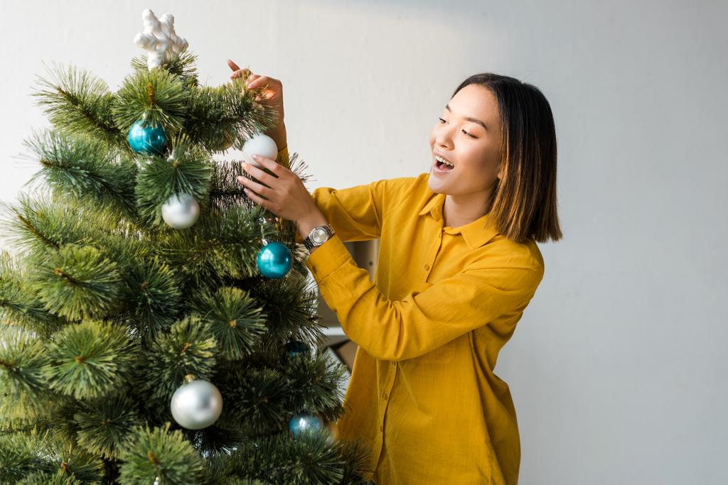 взволнованная азиатка украшает рождественскую елку в офисе
  - Фото, изображение
