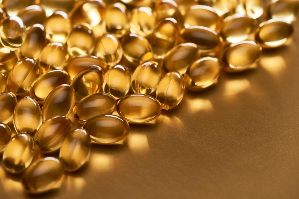 close-up zicht op glanzende visolie capsules op gouden achtergrond met kopieerruimte - Foto, afbeelding