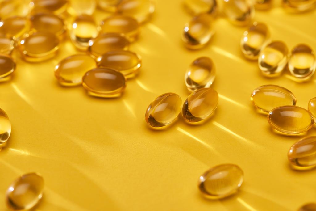 zblízka pohled na zlaté lesklé kapsle rybího oleje rozptýlené na žlutém jasném pozadí - Fotografie, Obrázek
