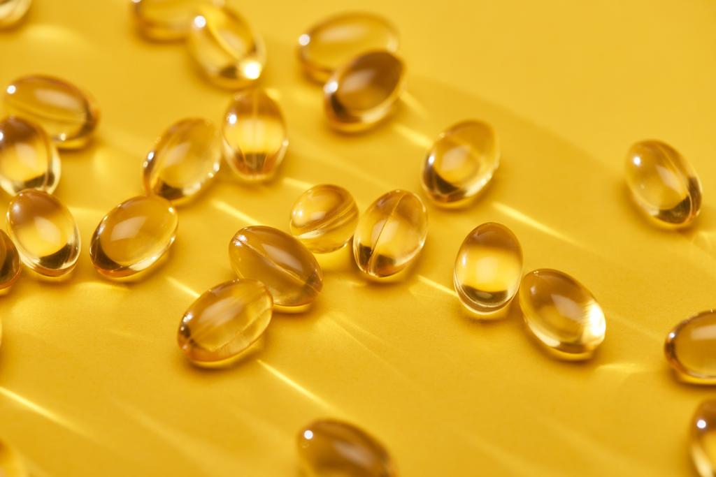 primo piano vista d'oro lucido capsule di olio di pesce sparsi su sfondo giallo brillante
 - Foto, immagini
