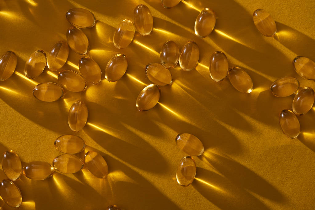 χρυσαφί κάψουλες ιχθυελαίου διάσπαρτες σε κίτρινο φόντο σε σκούρο - Φωτογραφία, εικόνα