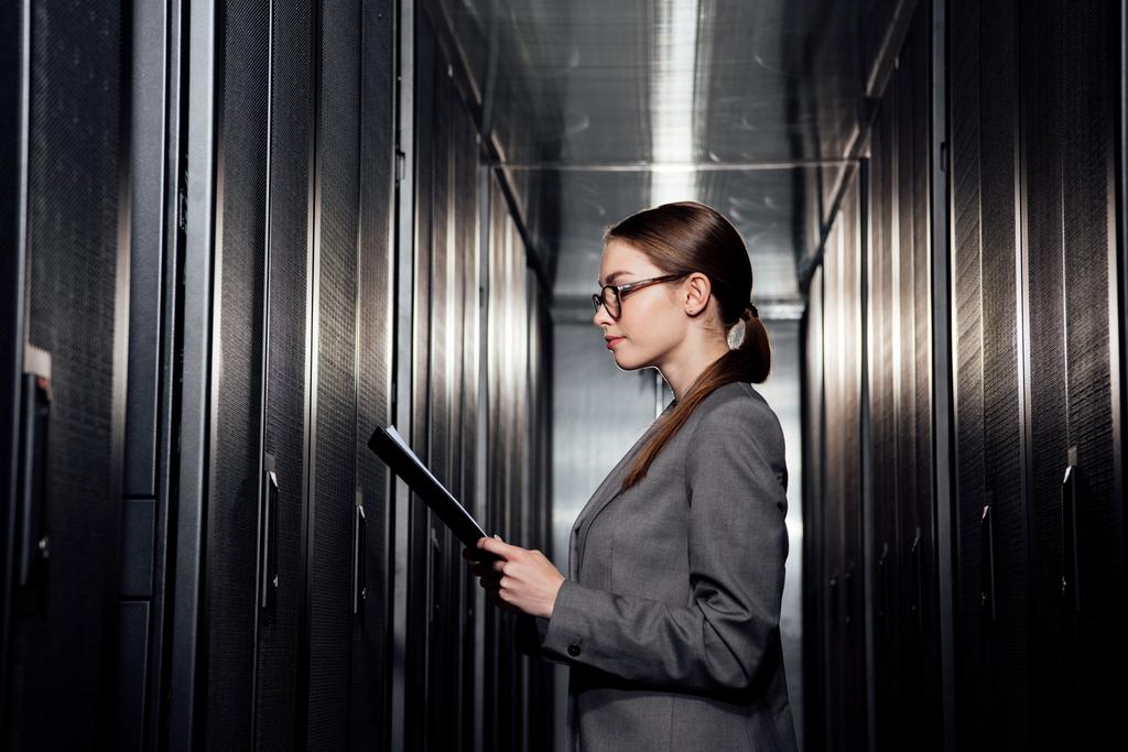 データセンターでクリップボードを保持しているメガネのビジネス女性の側面図  - 写真・画像