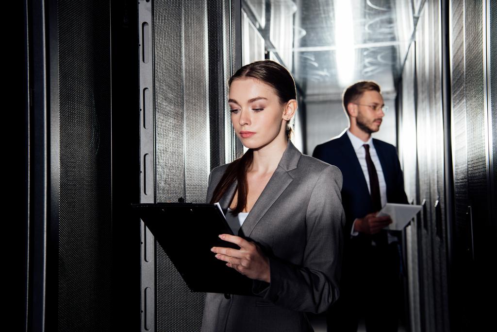 selective focus of attractive businesswoman holding clipboard near businessman in data canter  - Photo, Image