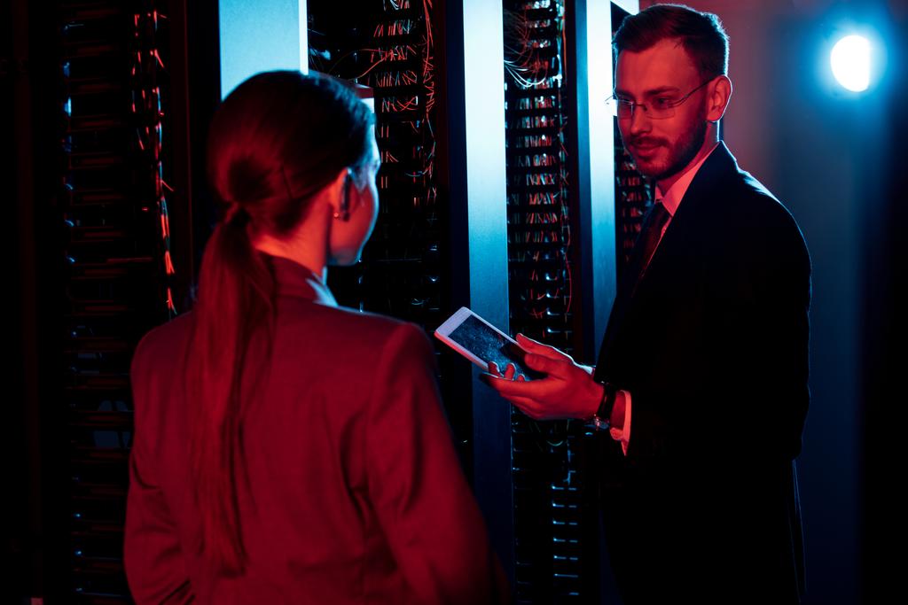 selective focus of handsome bearded businessman holding digital tablet near woman in server room  - Photo, Image