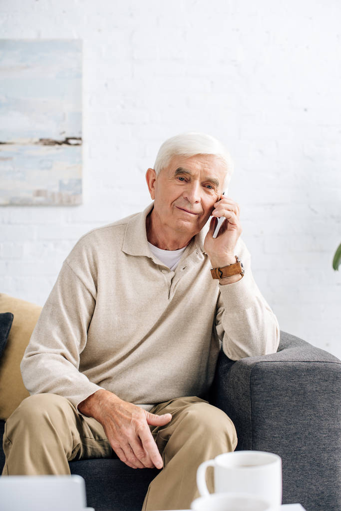 homme âgé souriant assis sur le canapé et parlant sur smartphone dans l'appartement
  - Photo, image