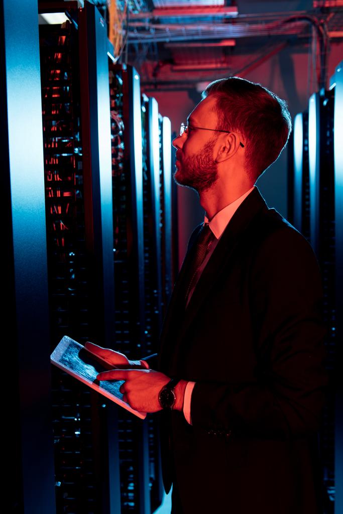 side view of bearded man in glasses holding digital tablet in server room  - Photo, Image