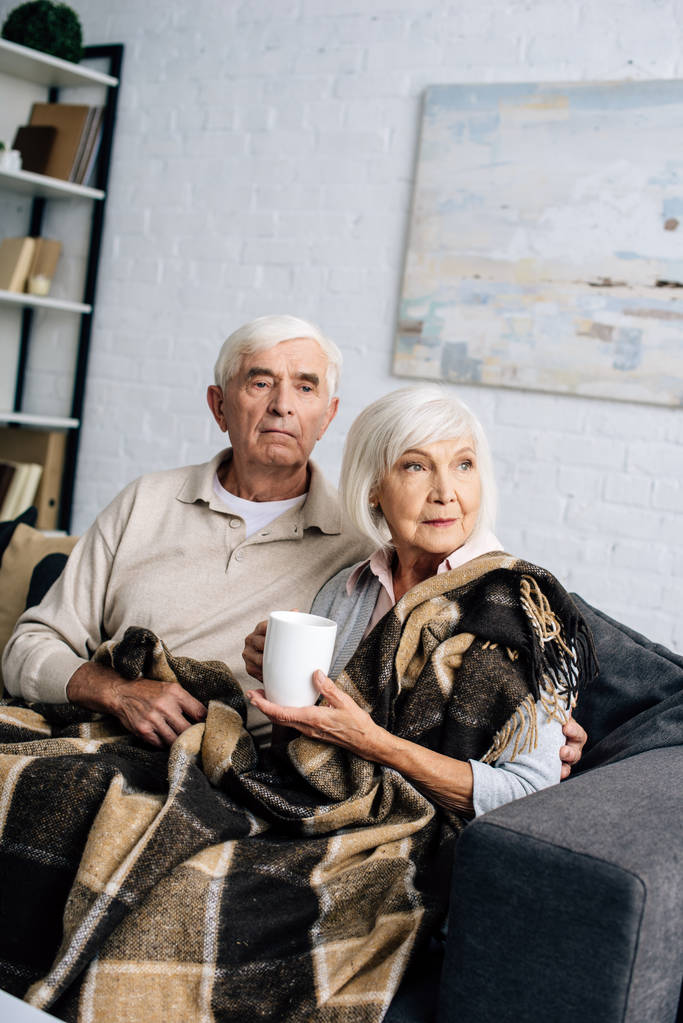 marito e moglie con tazza seduti sul divano e distogliendo lo sguardo in appartamento
  - Foto, immagini