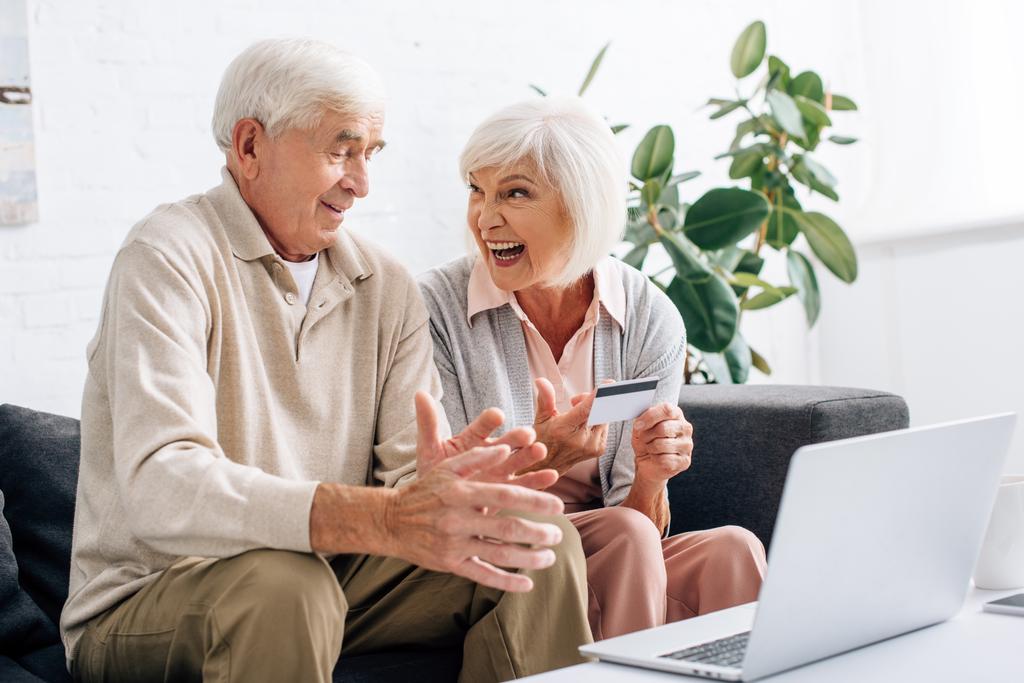 улыбающиеся муж и жена с помощью ноутбука и проведение кредитной карты в квартире
  - Фото, изображение