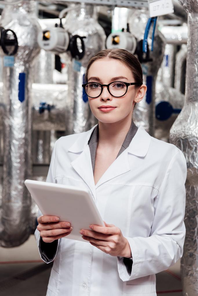 atraktivní inženýr v bílém plášti a brýlích držící digitální tablet v blízkosti vzduchového kompresního systému  - Fotografie, Obrázek