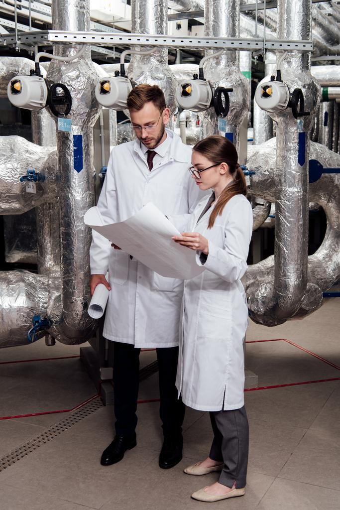 engineers in glasses and white coats looking at blueprint near air compressor system  - 写真・画像