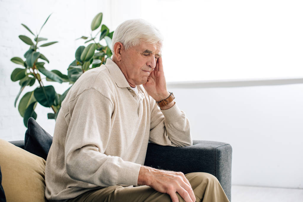 Senior sitzt auf Sofa und hat Kopfschmerzen in Wohnung  - Foto, Bild
