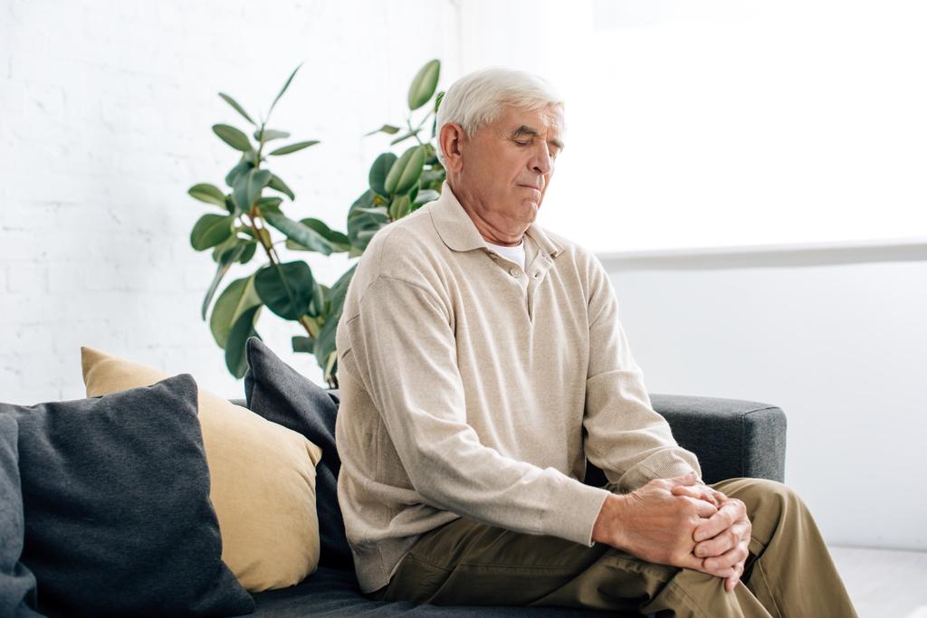 старший чоловік сидить на дивані і має коліно Артрит в квартирі
  - Фото, зображення