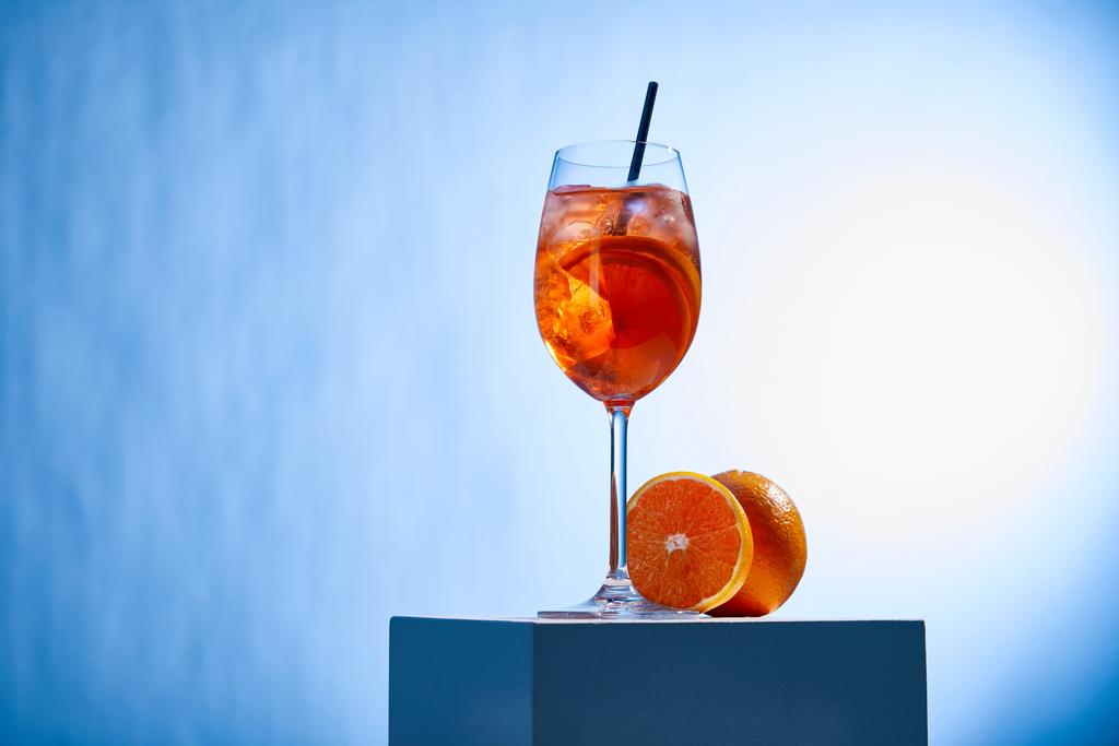 cocktail Aperol Spritz με καλαμάκι σε ποτήρι και πορτοκάλια σε μπλε φόντο  - Φωτογραφία, εικόνα