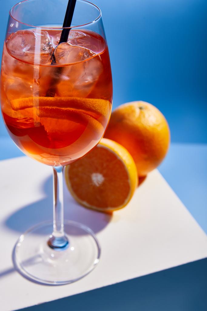 επιλεκτική εστίαση του κοκτέιλ Aperol Spritz με άχυρο σε ποτήρι και πορτοκάλια σε μπλε φόντο  - Φωτογραφία, εικόνα