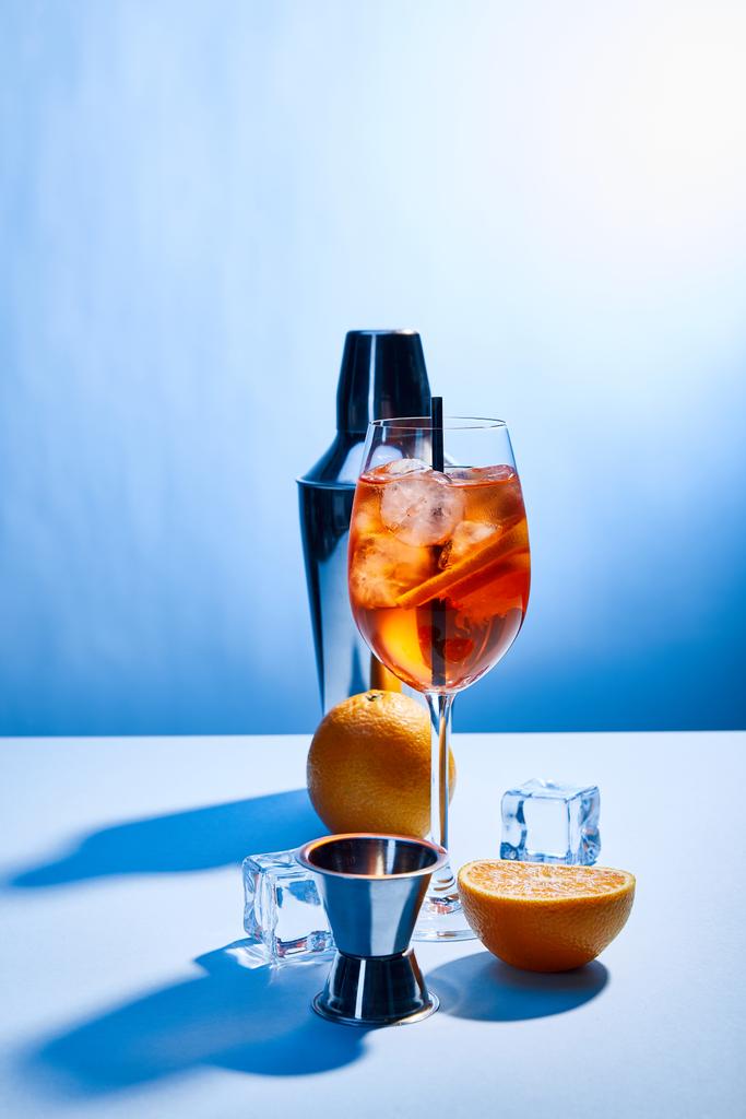 cocktail Aperol Spritz, sinaasappels, shaker, ijsblokjes en maatbeker op blauwe ondergrond  - Foto, afbeelding