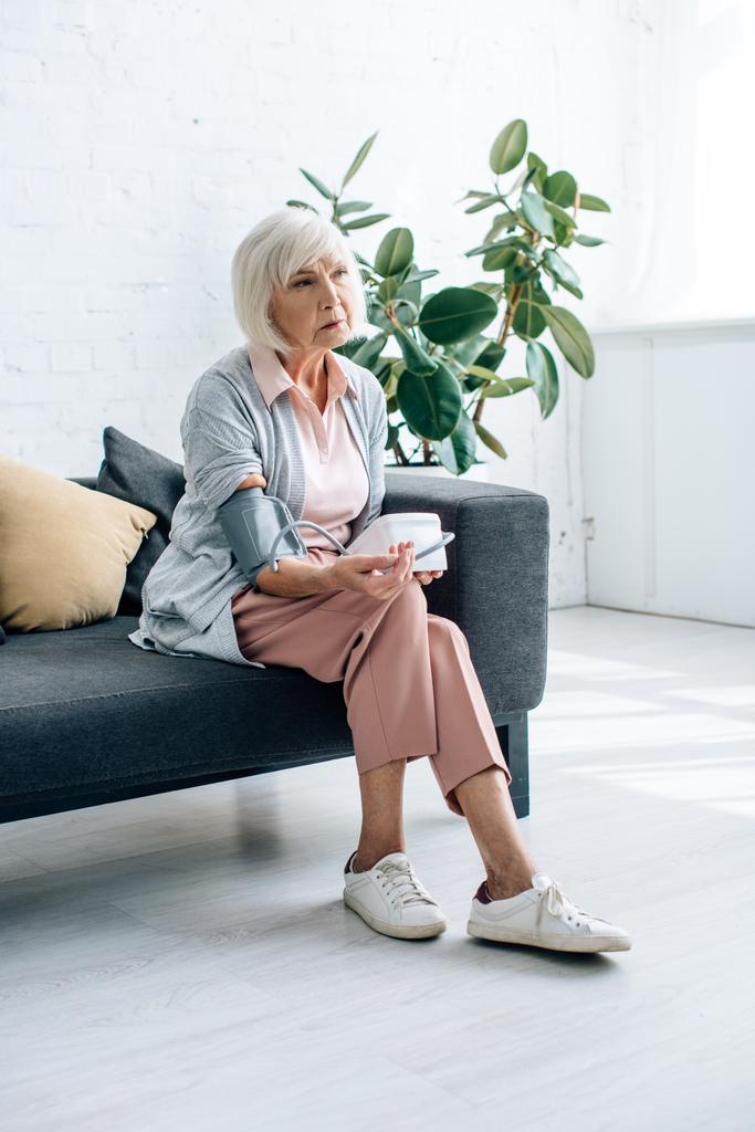 пожилая женщина сидит на диване и измеряет артериальное давление в квартире
  - Фото, изображение
