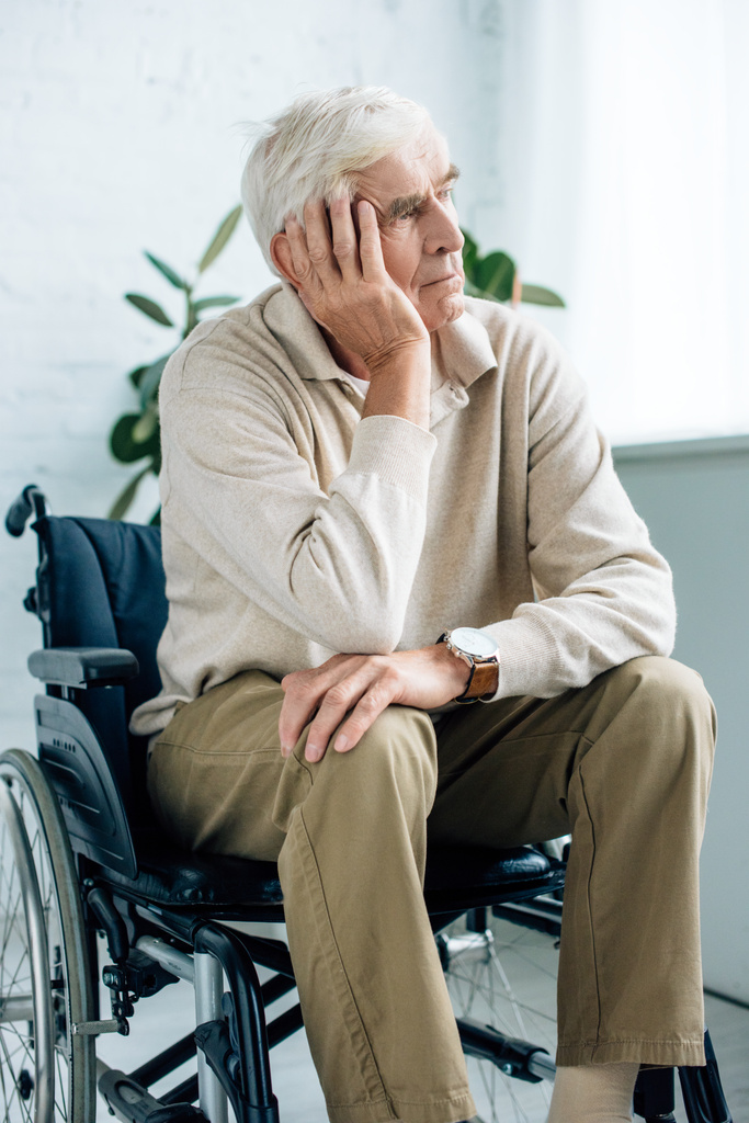 uomo anziano bello e sognante seduto in sedia a rotelle in appartamento
  - Foto, immagini