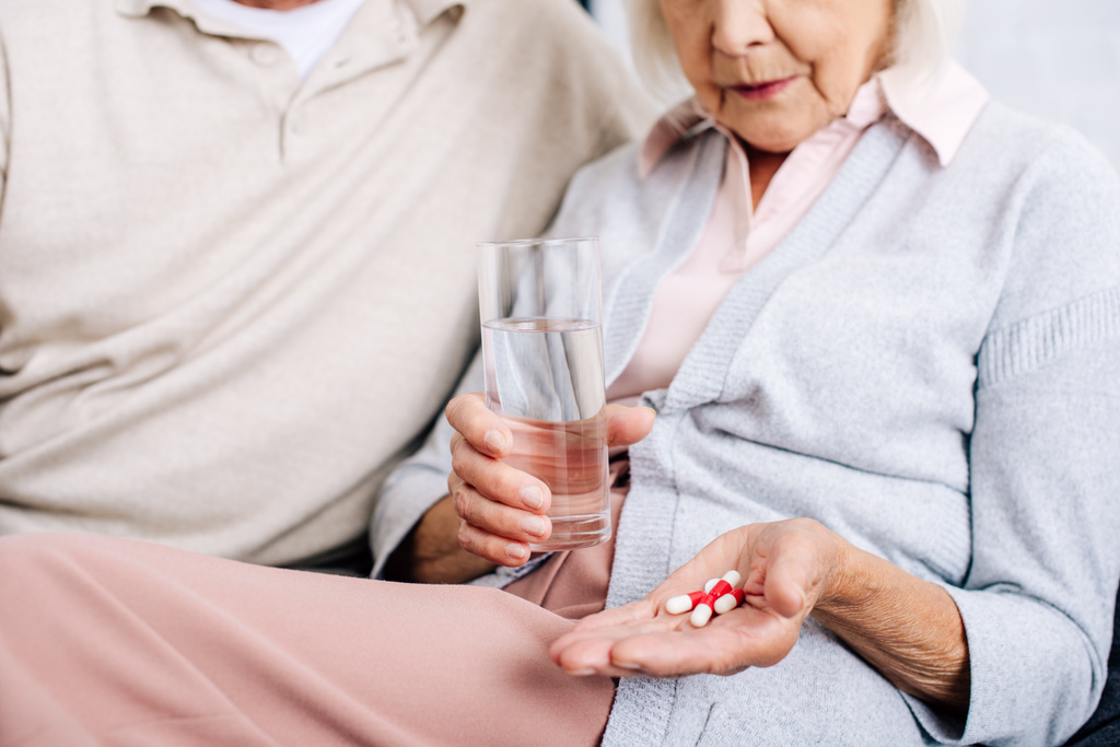 cropped view of husband and wife holding glass and pills in apartment  - Photo, Image