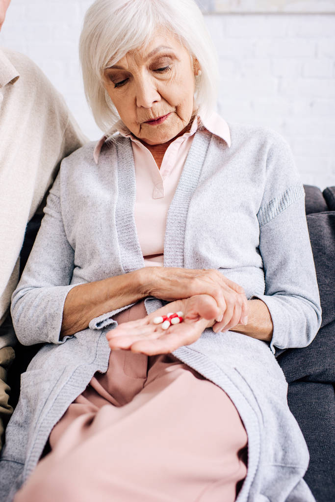 donna anziana seduta sul divano e in possesso di pillole in appartamento
  - Foto, immagini